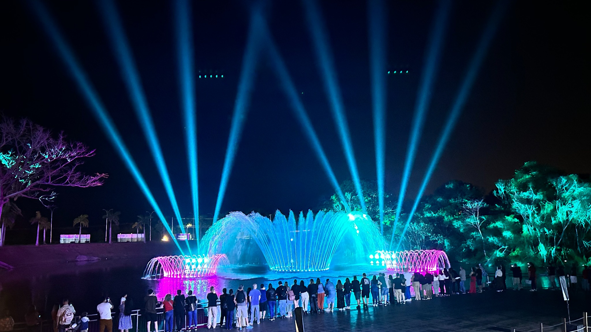 Show das Águas no Wonder Park Foz, com fontes iluminadas em azul e magenta, feixes de luz e visitantes acompanhando o espetáculo.